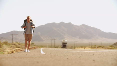 hombre de vacaciones haciendo autostop a lo largo de una carretera de campo filmado en r3d