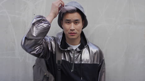 Porträt-Eines-Hübschen-Jungen-Asiatischen-Mannes,-Der-Seine-Haare-Repariert-Und-Eine-Stilvolle-Silberne-Jacke-Trägt,-Die-Selbstbewusst-Aussieht-Und-Den-Städtischen-Lebensstil-In-Zeitlupe-Genießt