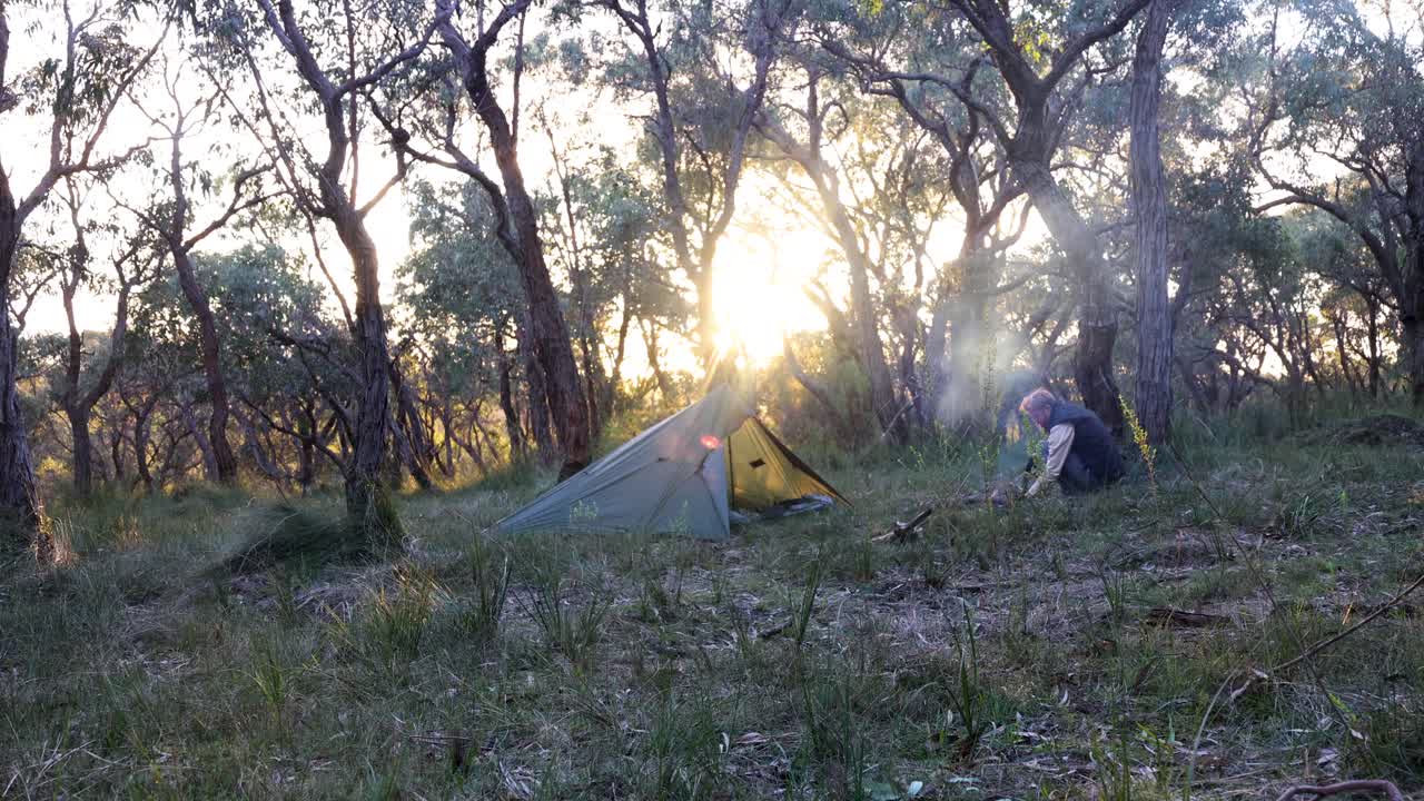 한 남자가 오스트레일리아의 숲에서 캠프 위에서 해가 지는 동안  ⁇ 고 있습니다.