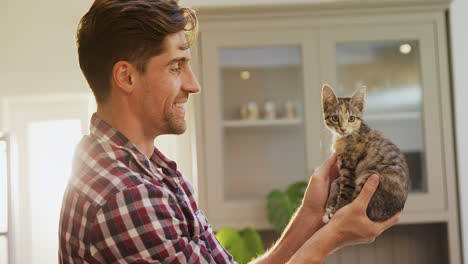 un joven sonriente sosteniendo a su gato mascota en sus manos en la cocina 4k 4k