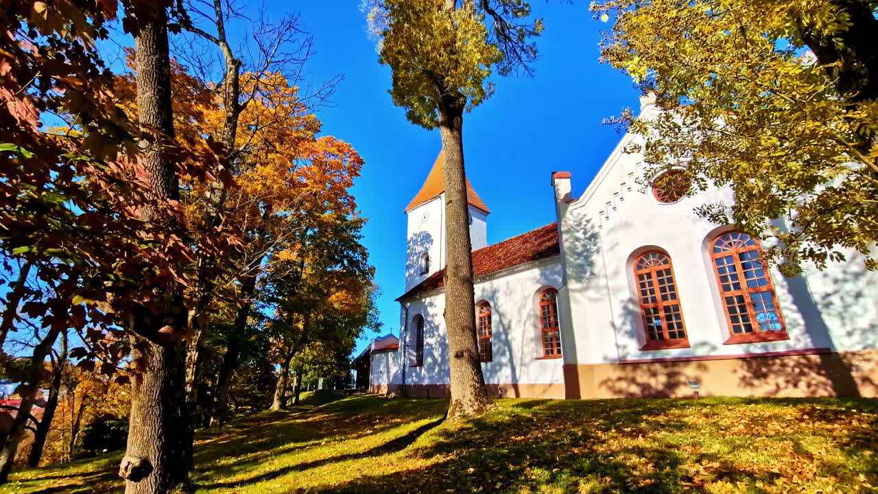 POV shot of walking towards a catholic church with tall trees surrounding in Talsi, Latvia