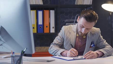 Handsome-and-stylishly-dressed-cultured-businessman-works-in-his-office-at-night,-taking-notes-on-his-agenda,-doing-research,-calculating.