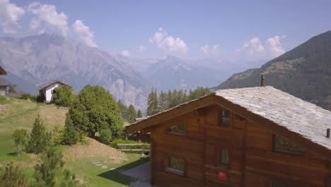 un drone de 4k filmado desde detrás de una cabaña suiza revelando las hermosas montañas y un pueblo en el fondo