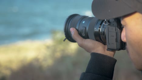 Nepali-filmmaker-with-camera-looking-through-viewfinder-at-coast