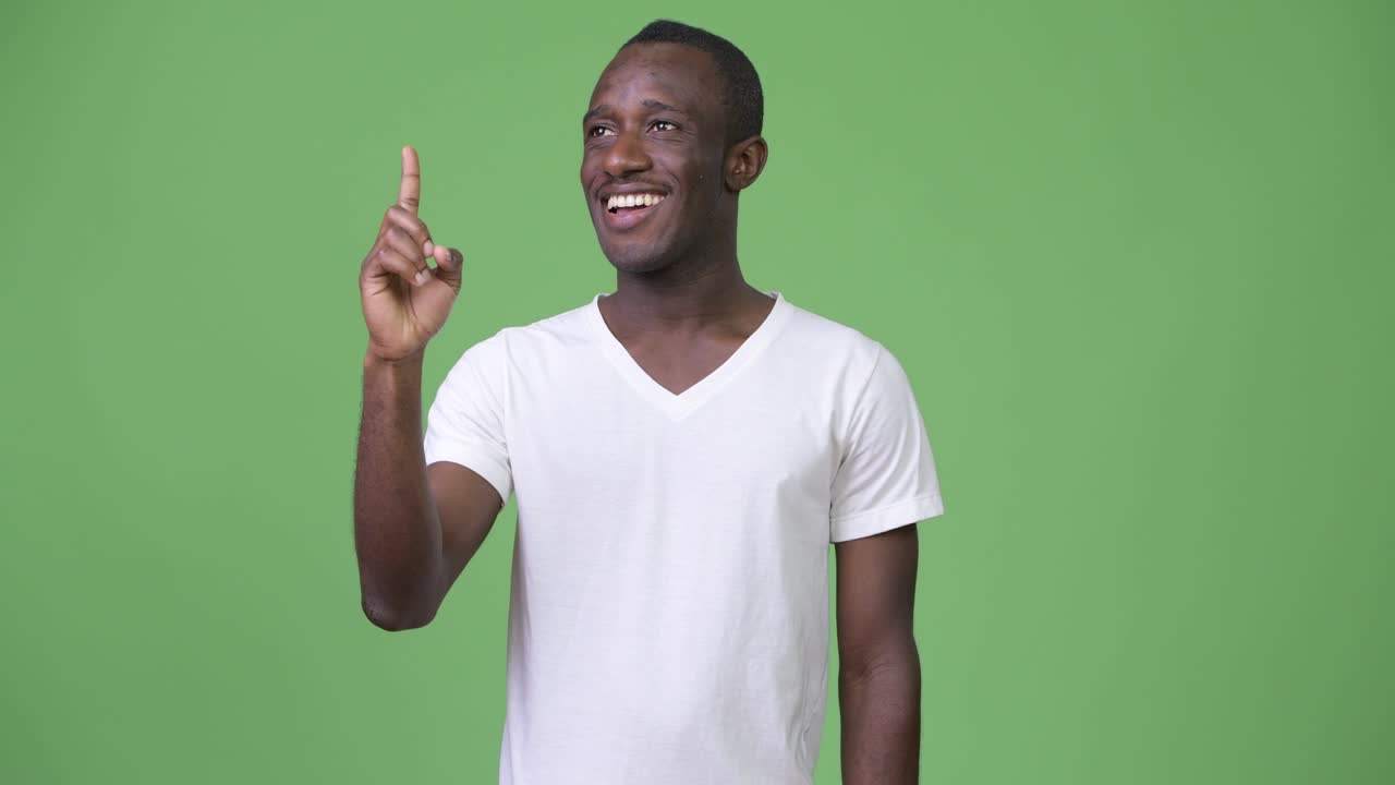 Ung glad afrikansk mand smilende og tænkende, mens han peger opad.