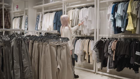 Fashion lover walks through bright clothing store, browsing racks of hanging tops and pants, inspecting fabrics and colors closely while choosing outfit in trendy spacious retail space