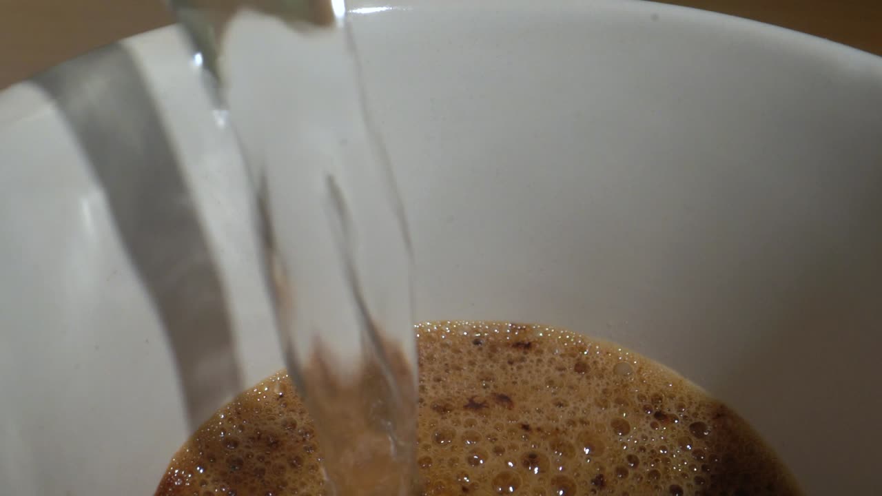 Extreme close-up of making instant coffee, hot water pouring into a mug of coffee granules.