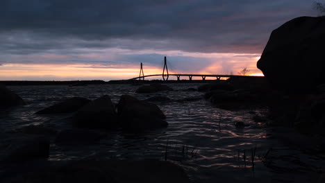 dark static shot of distant bridge by water, dramatic colorful sunset