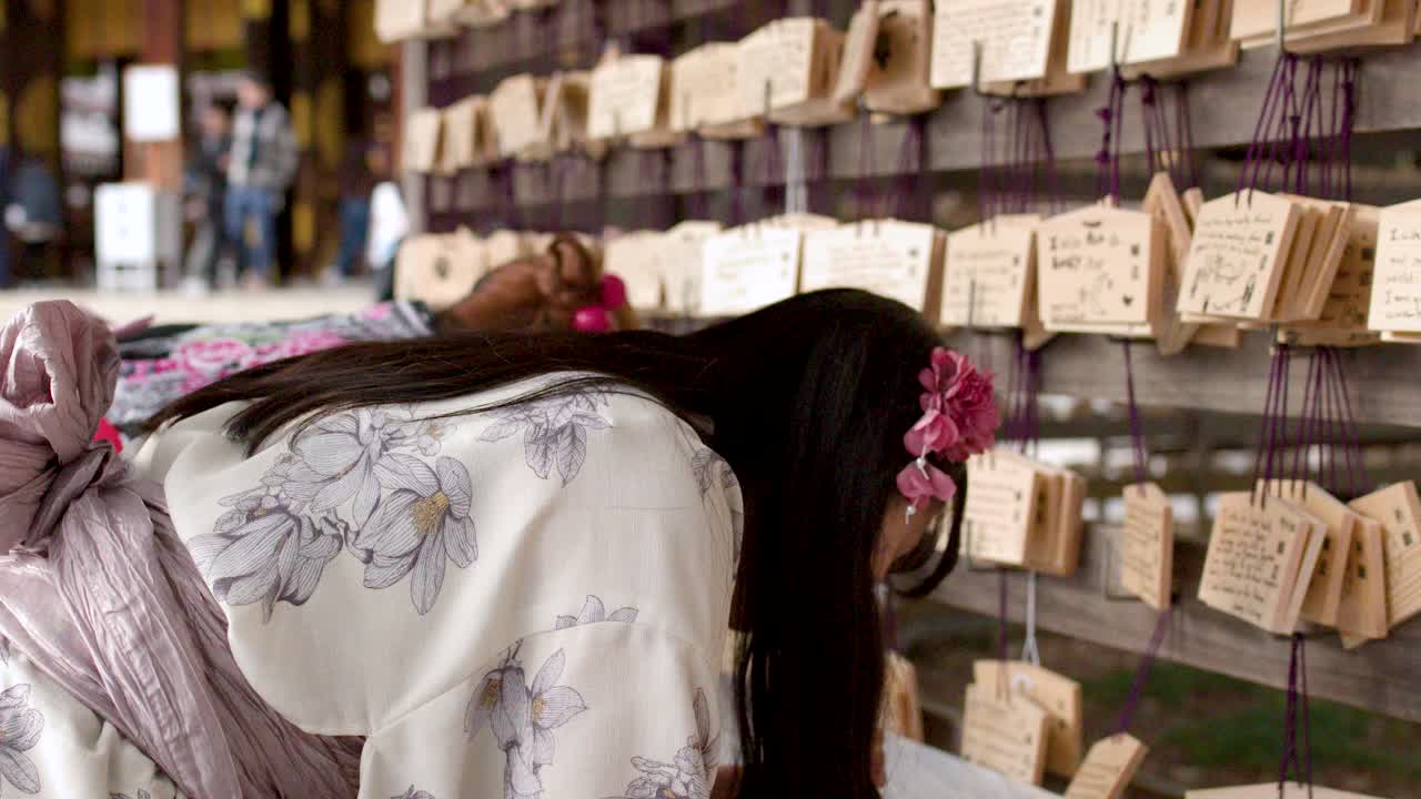 Uma mulher em quimono tradicional escreve em uma placa ema de madeira em um santuário xintoísta