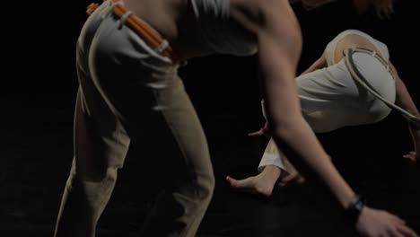 un grupo de bailarines profesionales están practicando capoeira en la oscuridad contra un foco de luz en un fondo negro de estudio. arte marcial afro-brasileño que combina elementos de la danza.