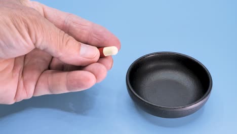 male hand takes a pill from a black cup standing on a blue surface