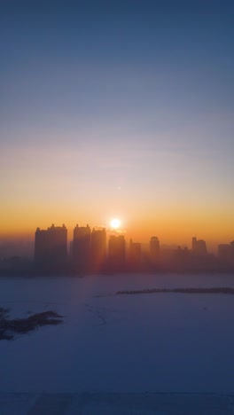 vertical aerial view of harbin’s skyline at sunrise, with golden sunlight illuminating the frozen songhua river, creating a stunning contrast between the icy landscape and the warm morning glow. china