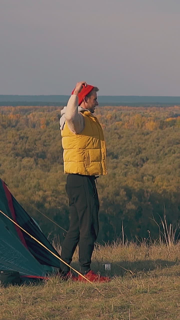 tourist gets out of blue tent and stretches near pretty girls on river bank meadow in early morning slow motion