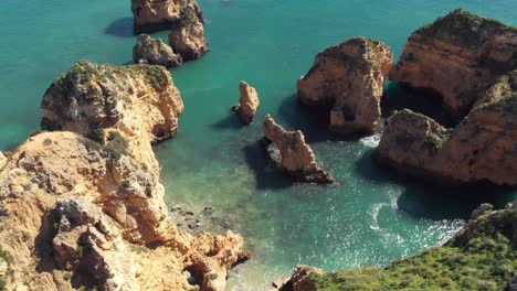 pointy golden rock formations sprouting from algarve blue sea in lagos, portugal - aerial top rotation view