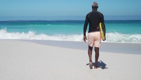 senior man walking with surfboard at the beach