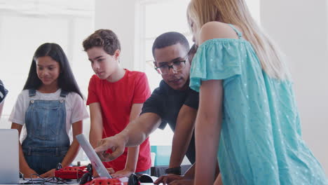 students with male teacher in after school computer coding class learning to program robot vehicle