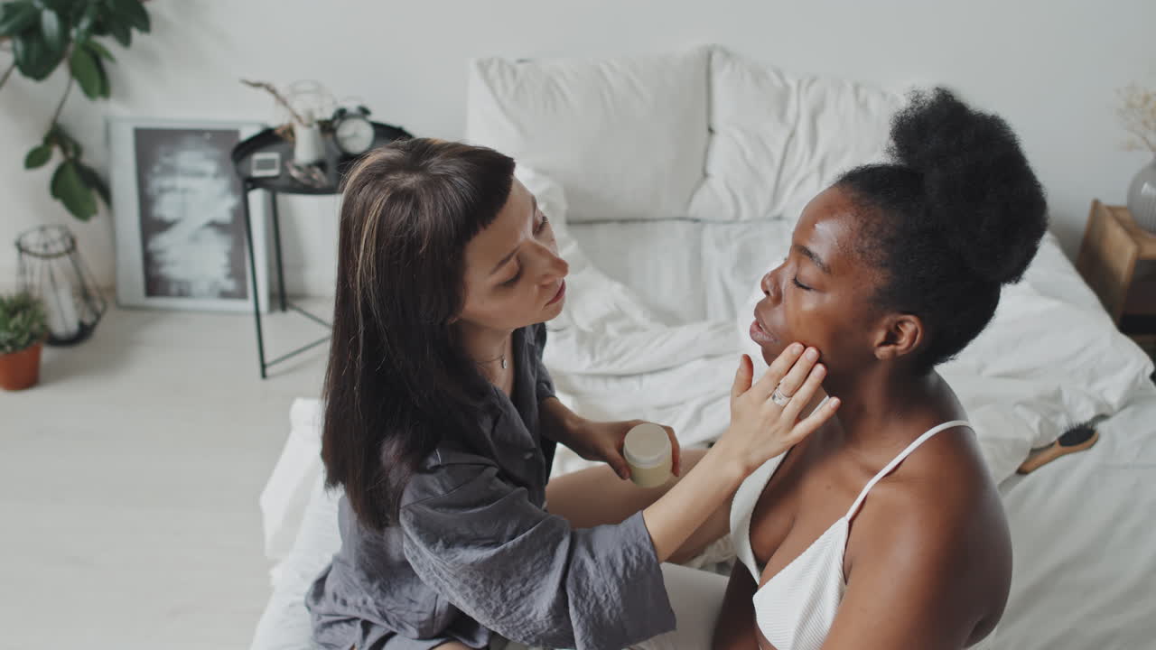 Young Woman Putting Cream on Girlfriends Face