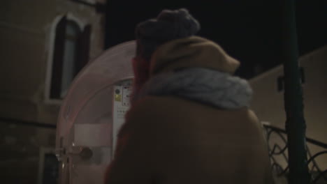 Woman-walking-in-night-city-and-talking-on-pay-phone