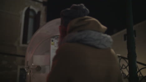 woman walking in night city and talking on pay phone