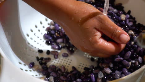 mano moviendo frijoles negros en colador para enjuagar en agua, cierre lento