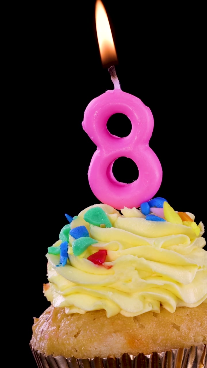 Un'inquadratura verticale di una candela rosa accesa a forma di numero otto sopra un cupcake giallo glassato.