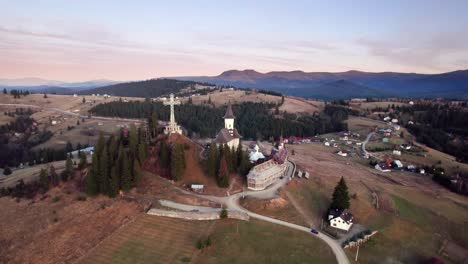 Vista-Aérea-De-Una-Iglesia-En-La-Cima-De-Una-Colina-En-El-Paisaje-Alpino-Al-Atardecer