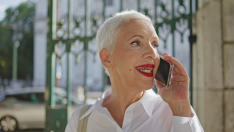 aged woman talking mobile phone outdoors closeup. joyful pensioner in sunlight