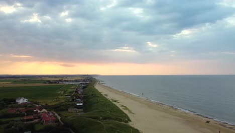 Aerial---Flying-backwards-over-an-empty-beach-in-Norfolk-at-sunset,-England