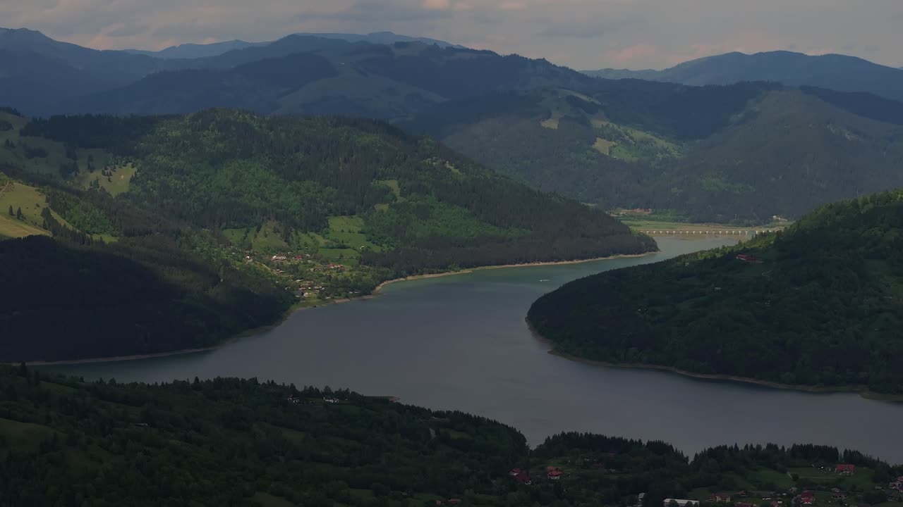 공중에서 가까이 찍은 사진은 녹색, 숲으로 둘러싸인, 부분적으로 구름이 많은 호수를 보여줍니다.
