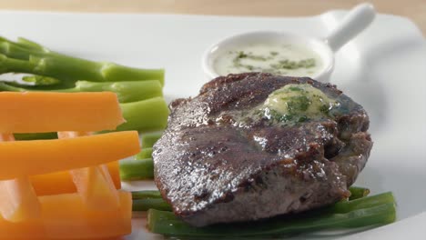 close shot of garlic and herb butter melting on a steak with vegetables on a white plate