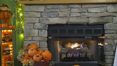 a view of a fireplace with a fire, all decorated for autumn with pumpkins, scarecrows and fall leaves