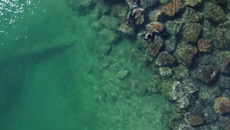 Einzigartige-Rotierende-Ansicht-Von-Zwei-Personen,-Die-Im-Tiefen-Wasser-Neben-Einer-Künstlichen-Struktur-Aus-Großen-Felsbrocken-Schnorcheln