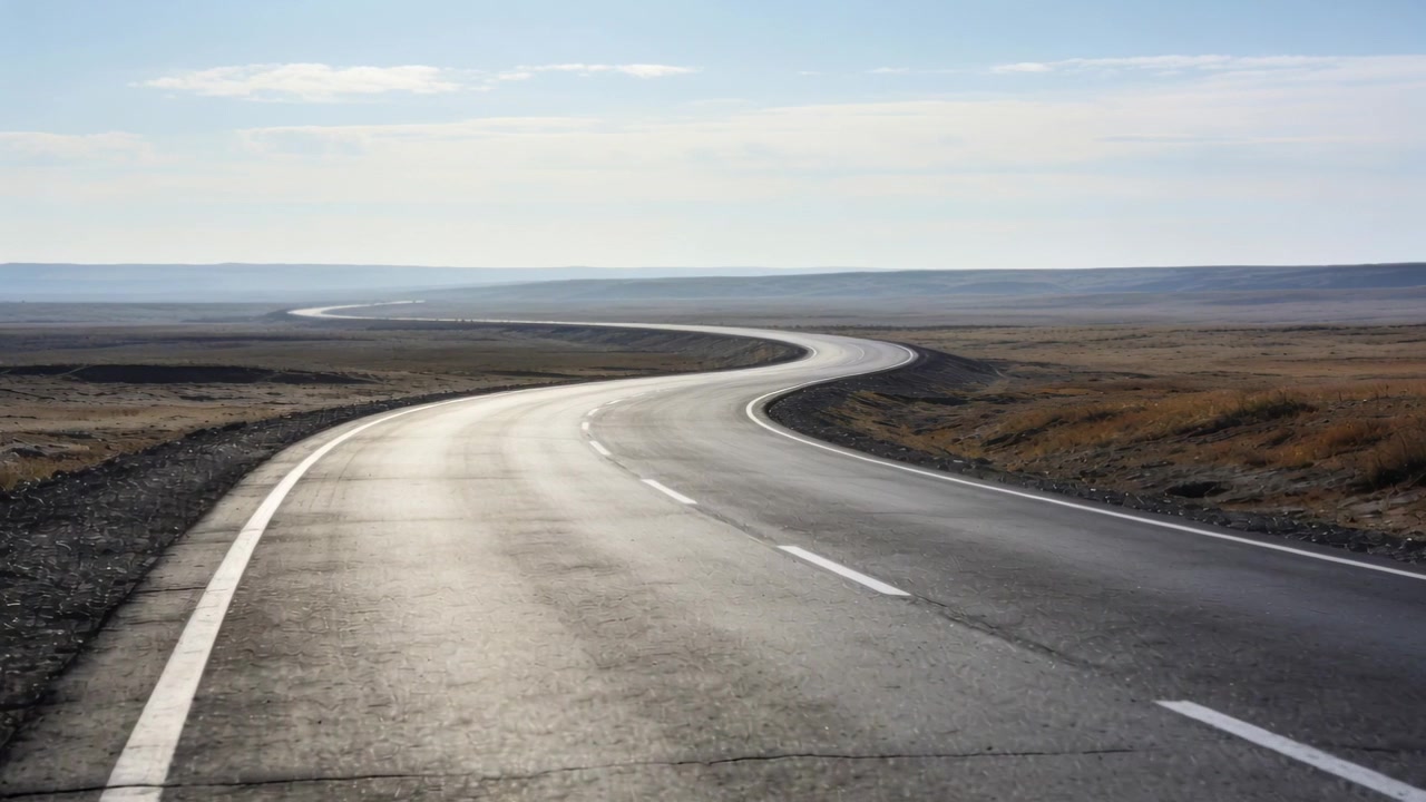 Autostrada curva con linee centrali tratteggiate che si estende verso una cresta attraverso la pianura, con la luce solare che cambia.