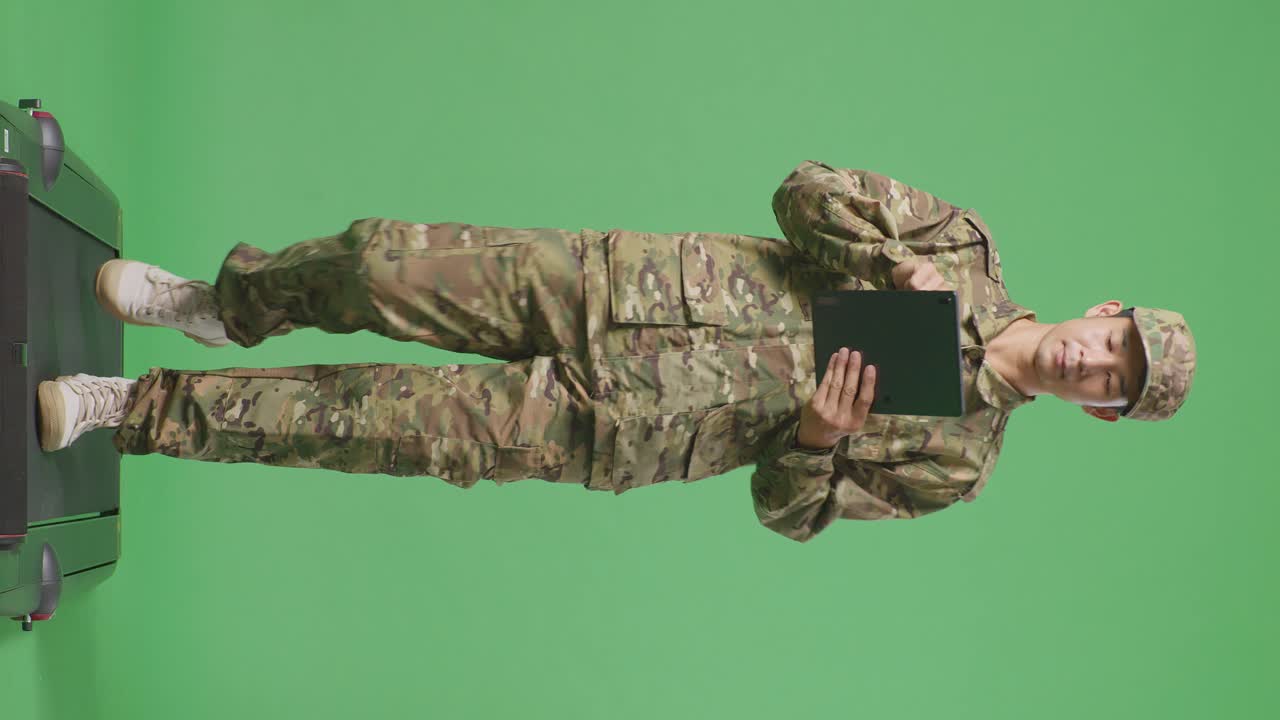 cuerpo lleno de soldado hombre asiático usando una tableta mientras caminaba en el estudio de fondo de la pantalla verde