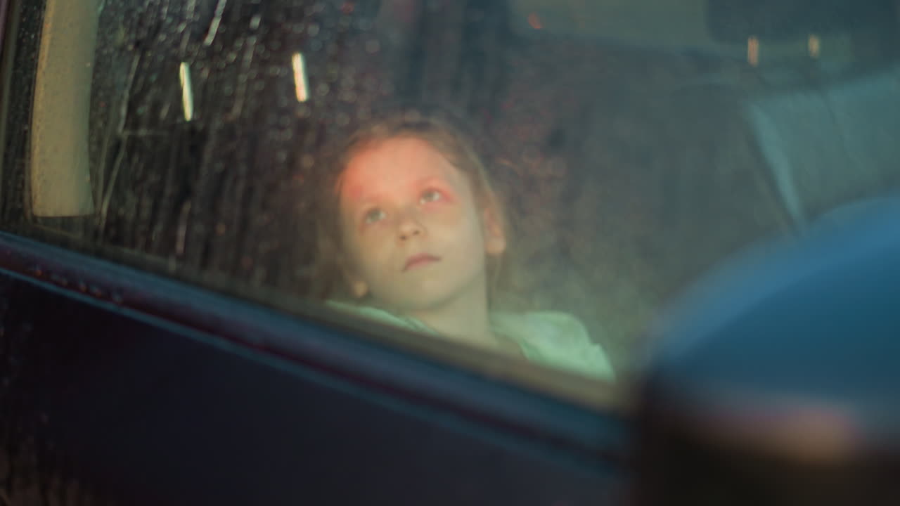 한 비가 오는 날 차에 타고 다니는 어린 소녀는 부정적인 감정을 표현합니다.