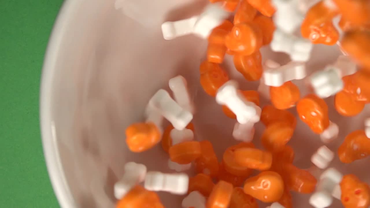 caramelos con forma de calaveras y huesos naranjas que caen sobre un plato