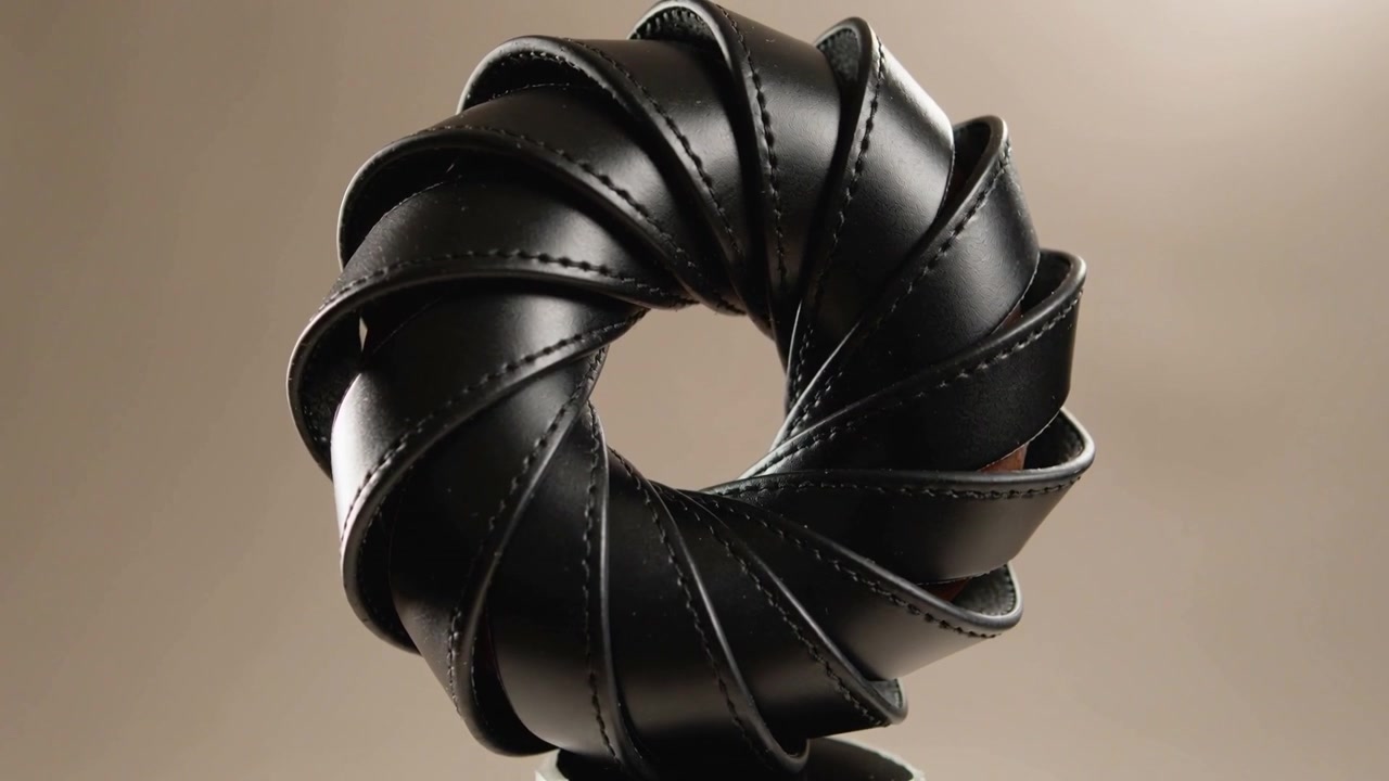 Motor engaging, rotating torus leather ring showing stitching on pedestal in studio for catalog