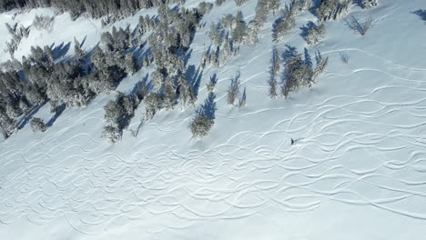 drone shot of snowboarder riding on board down the snowy mountain hill on sunny day