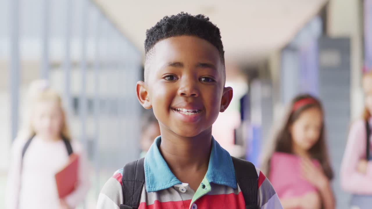 Ritratto di scolaro afroamericano felice che cammina nel corridoio della scuola.