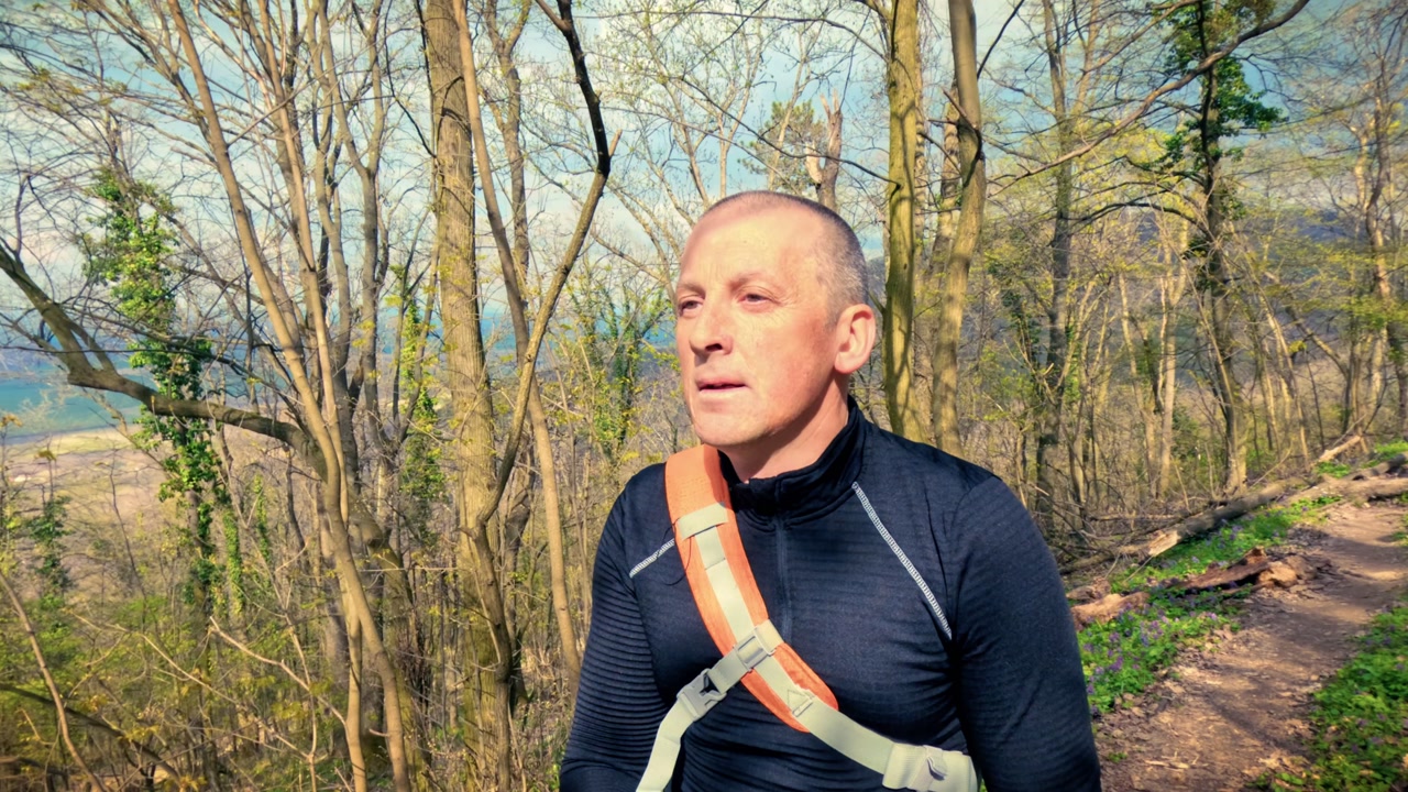 Authentic mature man walking through a blooming spring woodland path with purple flowers. Promoting personal health, fitness, mental well-being, and the calming power of nature for stress relief.