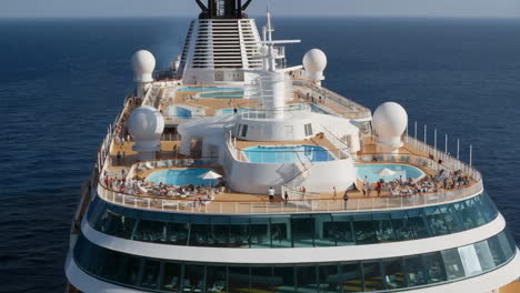 top deck of a luxury cruise ship with pools and sunbathers at sea