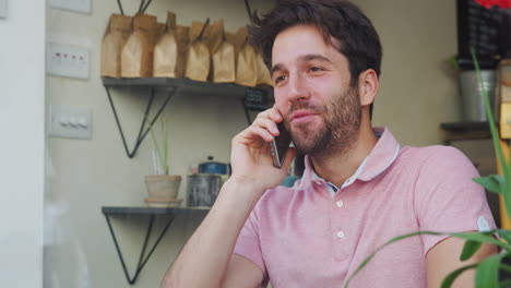 un joven en una cafetería hablando por teléfono móvil