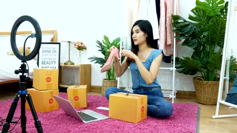 4k. asian woman live streaming for selling shoe, fashion accessories online on social media via mobile phone from bedroom at home. owner of small business working from home during self isolation