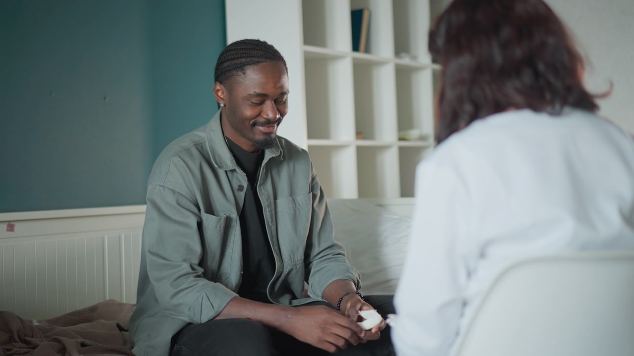 Mann som møter helsepersonell under konsultasjon. Hjemmeklinikkmiljø med sykepleier som utfører mental screening og rådgivning, oppmerksom lytting, pasientsmil, nattbordslampe, konfidensielt