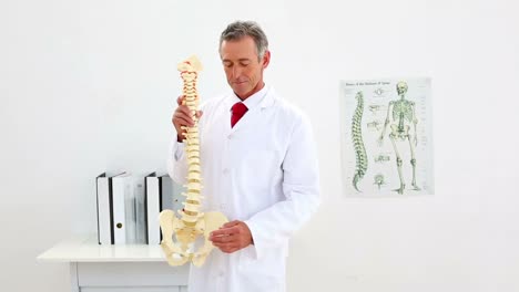 un médico sonriente explicando el modelo de la columna vertebral a la cámara