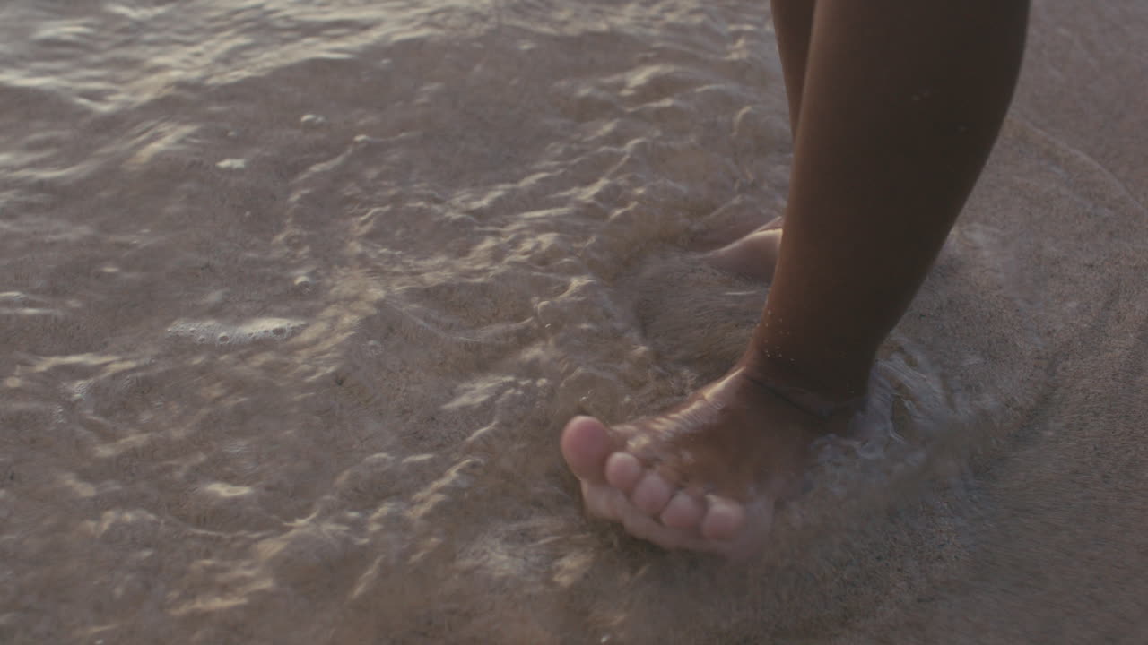 Close up of a gentle wave washing on child's feet standing on sand