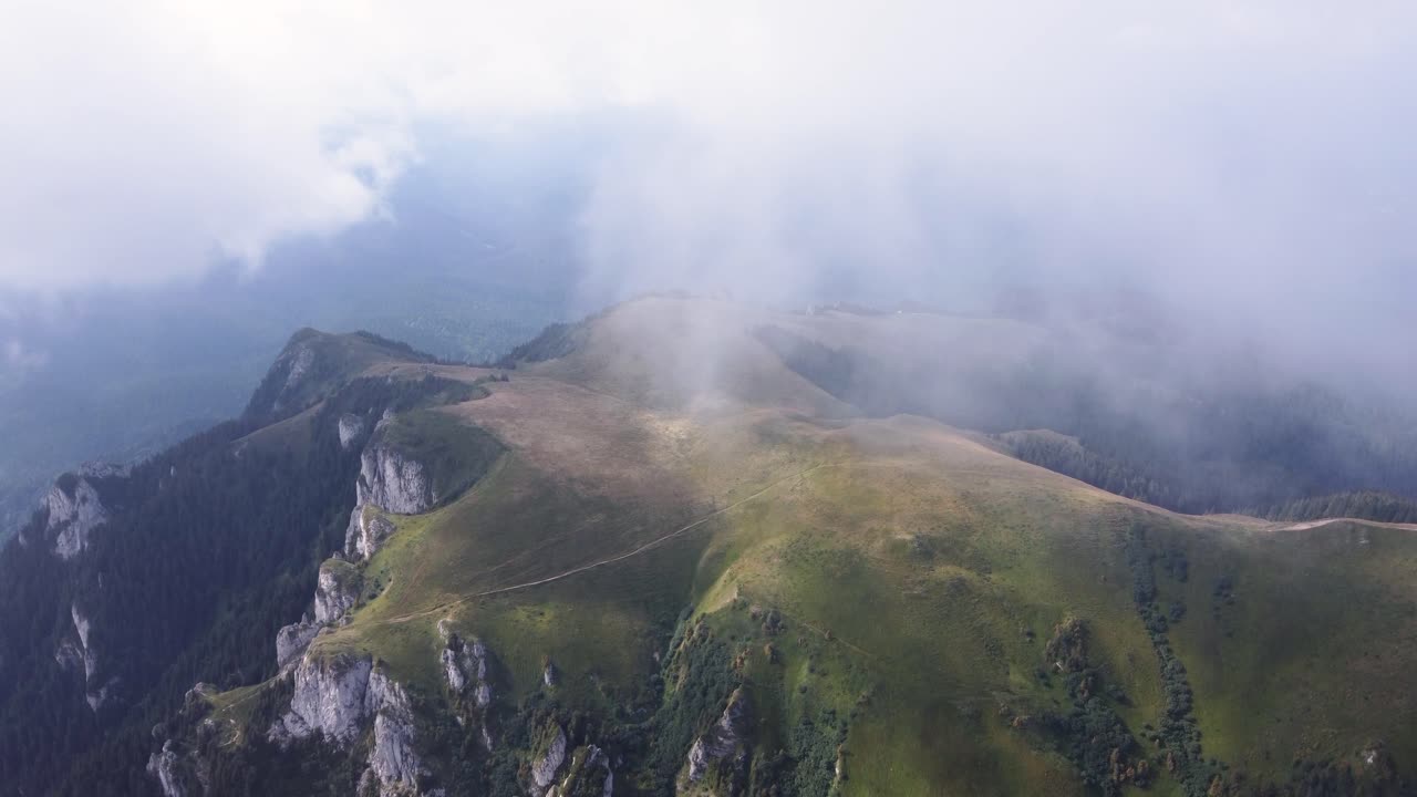 Experience the mystique of a mountain peak covered in summer mist, captured from a mesmerizing drone's perspective