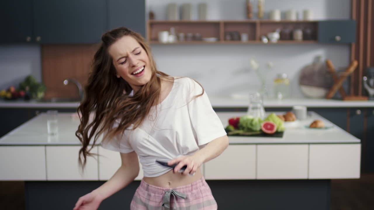 Donna entusiasta che balla con la cucina sullo sfondo. Casalinga che si diverte in casa.