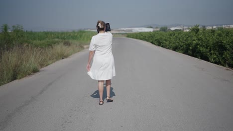woman walking on a country road taking photos with tablet