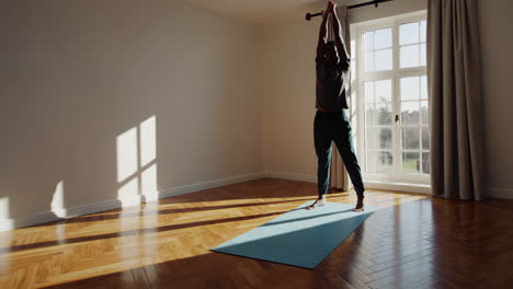 man exercising and stretching on yoga mat in sunny room